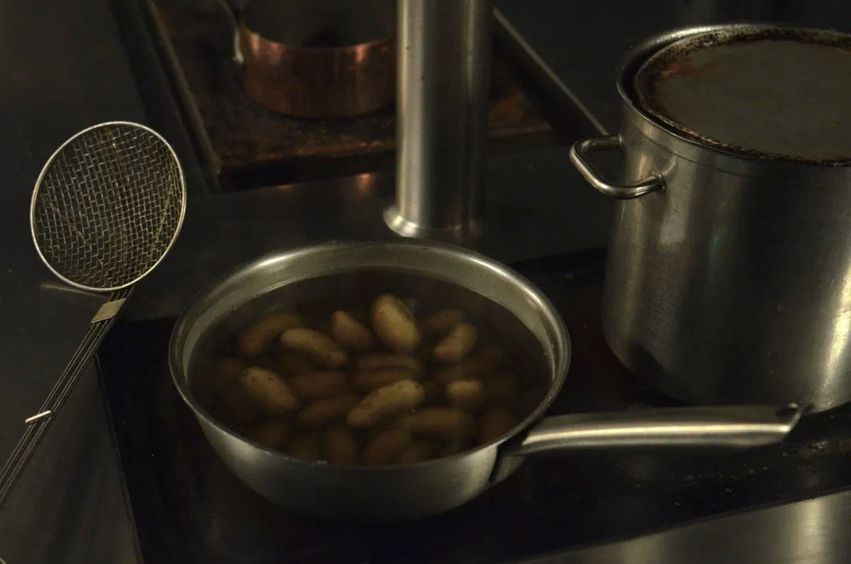 Petites pommes de terre entières avec leur peau, couvertes d'eau dans une casserole en inox posée sur le feu, à côté d'une écumoire
