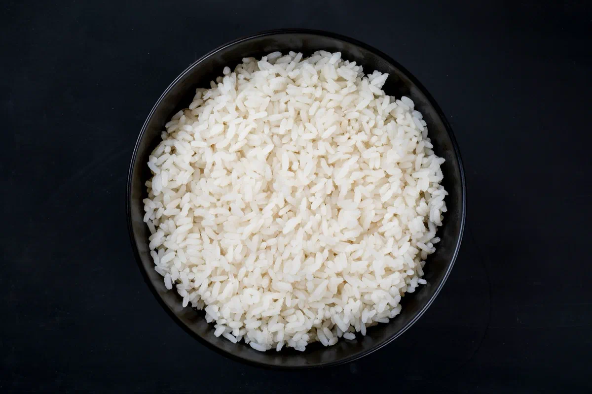 Un bol noir rempli de riz blanc cuit aux grains bien détachés, vu de dessus sur un fond sombre