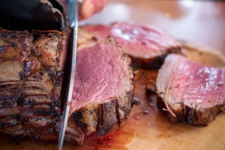 Un rôti de bœuf découpé au couteau sur une planche, les tranches rosées au cœur et bien saisies sur le pourtour