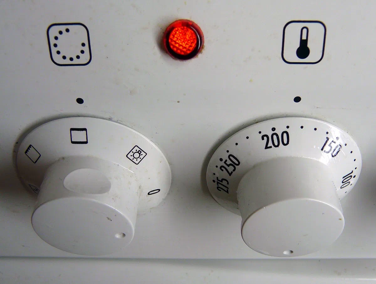 Les boutons d'un four électrique blanc, celui de droite gradué en degrés Celsius de 50 à 250, voyant de chauffe allumé