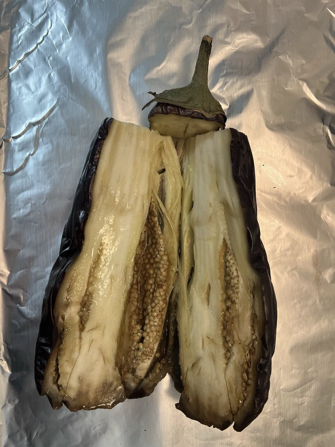 Une aubergine rôtie ouverte en deux dans la longueur, chair fondante et peau violette plissée, posée sur une feuille d'aluminium