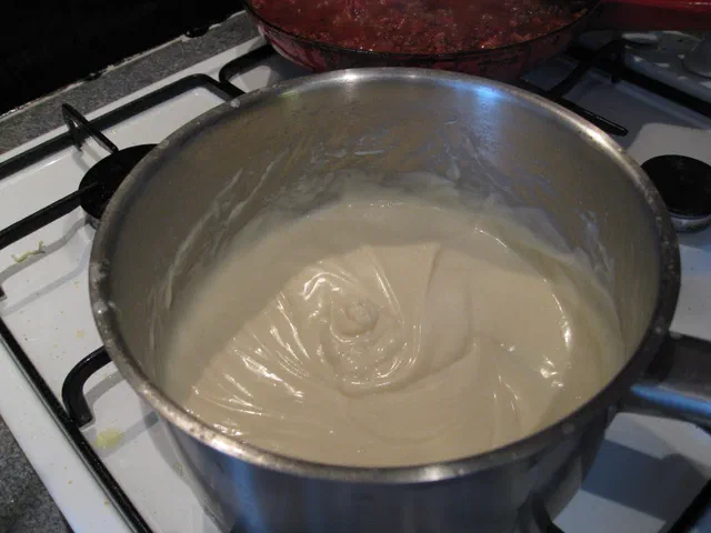Une casserole en inox remplie de béchamel épaisse et lisse, posée sur une gazinière