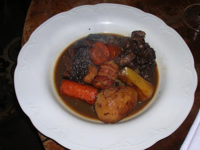 Bœuf bourguignon dans une assiette creuse blanche, morceaux de bœuf en sauce sombre au vin avec des carottes, des lardons et une pomme de terre