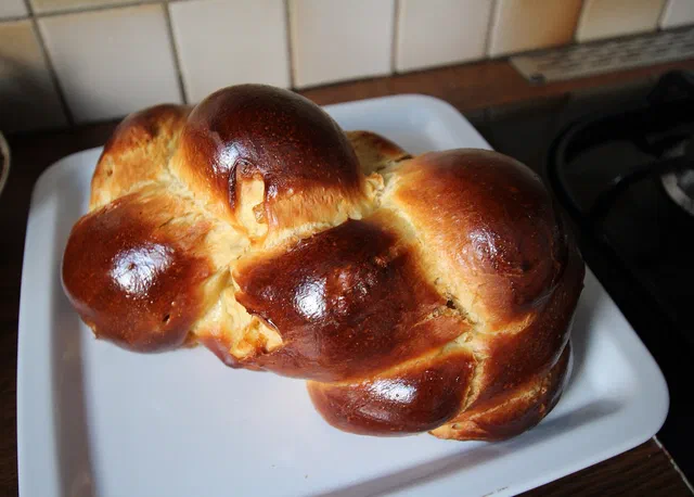 Une brioche tressée bien dorée et brillante posée sur un plat blanc