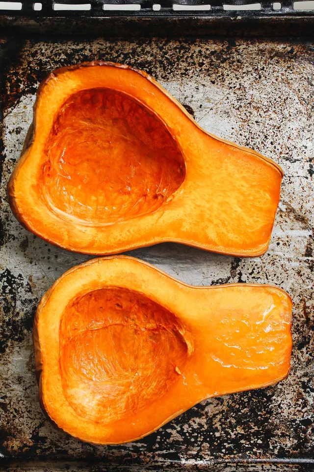 Deux moitiés de courge butternut rôties au four, vidées de leurs graines, chair orange brillante, sur une plaque de cuisson en métal patinée