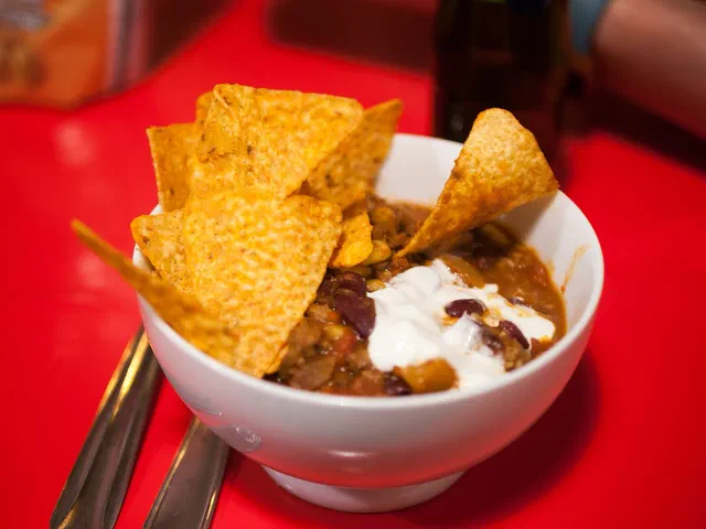 Bol blanc de chili con carne aux haricots rouges, garni de crème fraîche et de chips de maïs, sur une table rouge