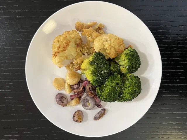 Une assiette de fleurettes de chou-fleur dorées, de bouquets de brocoli, d'oignons rouges et de gousses d'ail rôtis