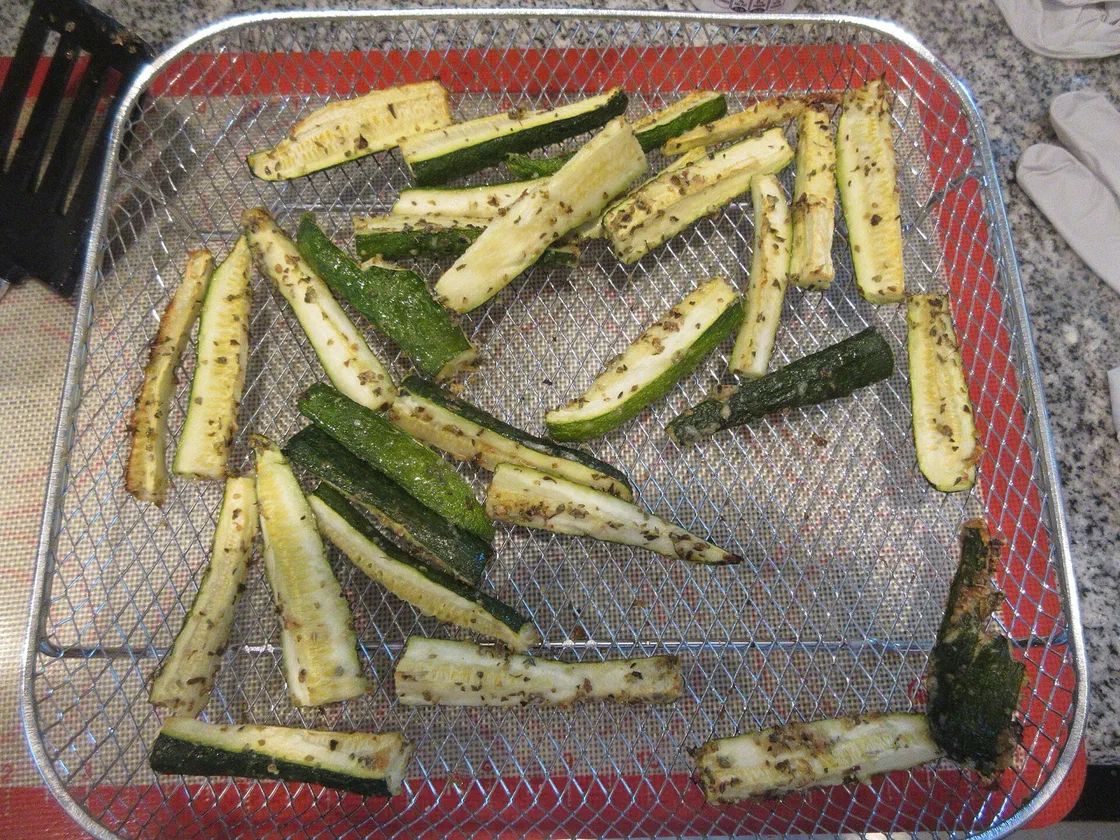 Bâtonnets de courgette rôtis aux herbes, peau verte et chair dorée, étalés dans le panier grillagé d'un air fryer