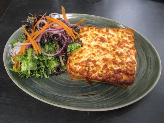 Un croque-monsieur au fromage gratiné et doré servi sur une assiette avec une salade de crudités