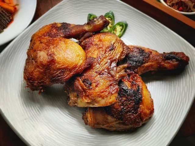 Trois cuisses de poulet entières à la peau dorée et grillée par endroits, sur une assiette blanche, avec quelques rondelles de piment vert