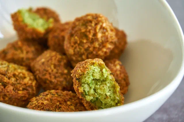 Des falafels dorés dans un bol blanc, l'un d'eux ouvert montrant l'intérieur vert aux herbes