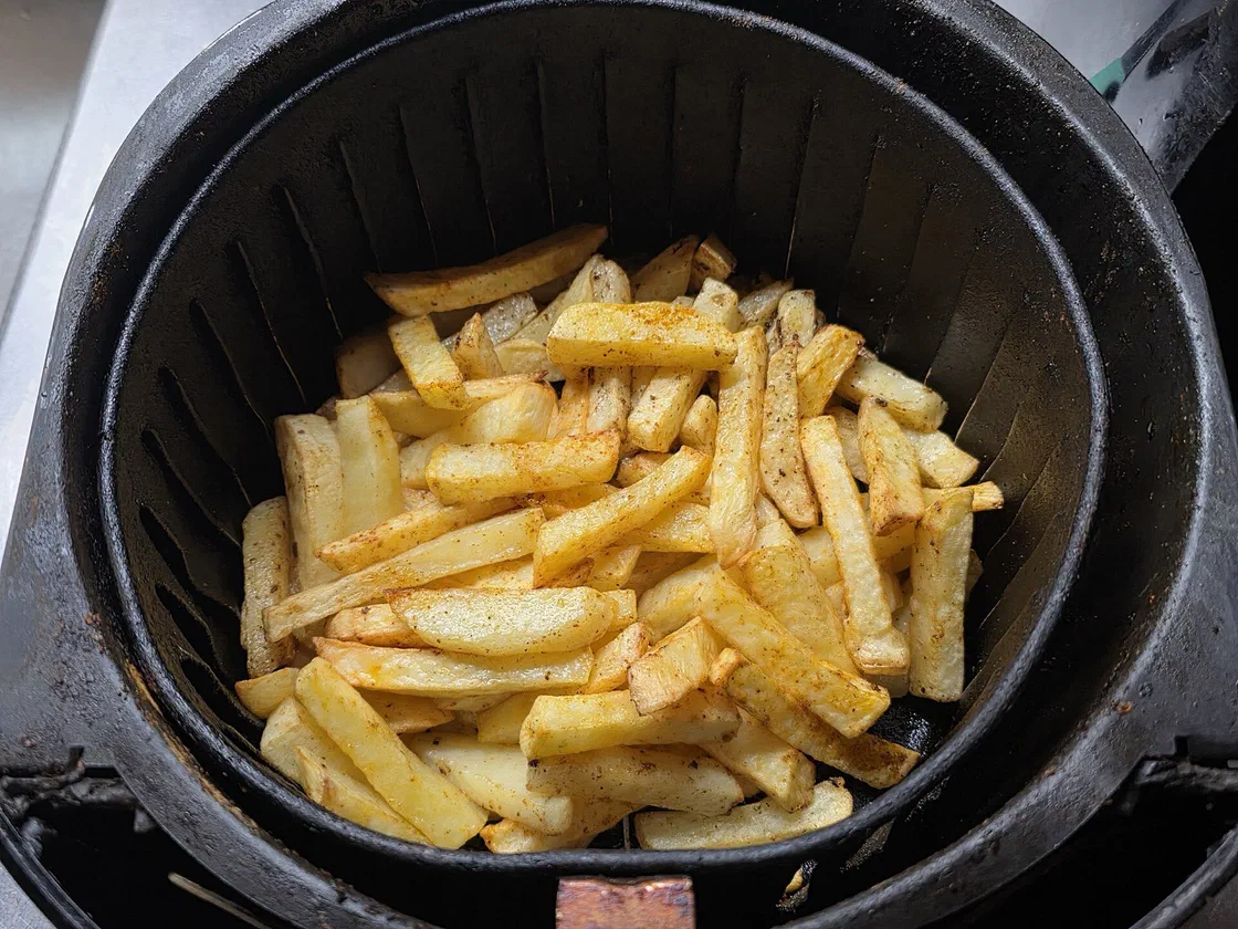 Frites maison dorées dans le panier noir d'un air fryer, vues du dessus
