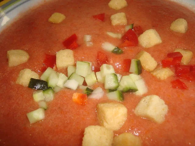 Un gaspacho orangé vu de dessus, garni de petits dés de concombre, de poivron rouge et de croûtons