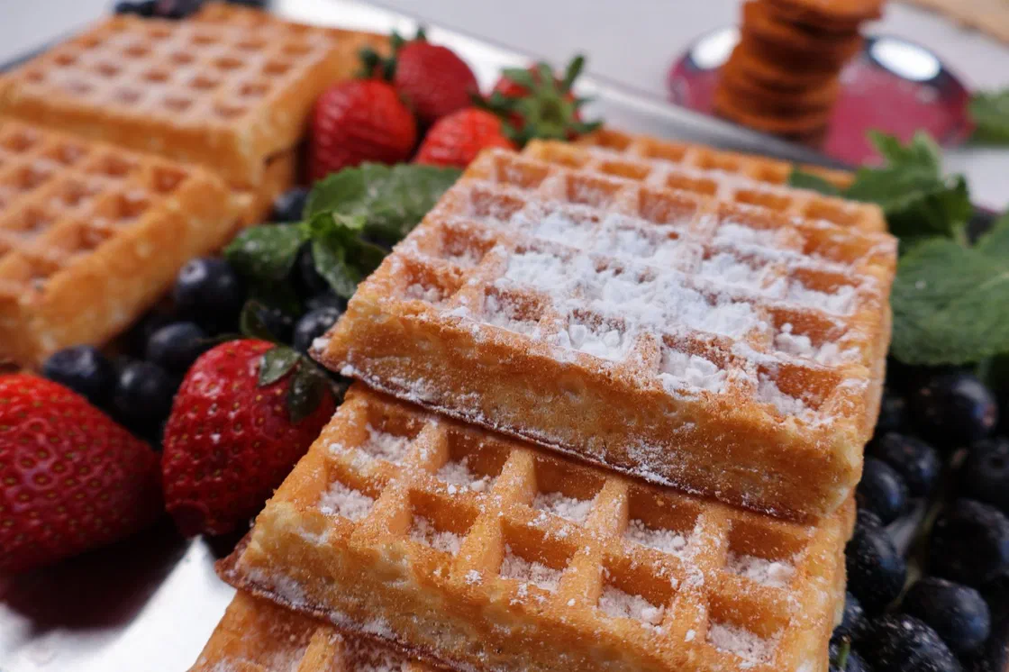 Gaufres rectangulaires dorées saupoudrées de sucre glace, entourées de fraises, de myrtilles et de feuilles de menthe