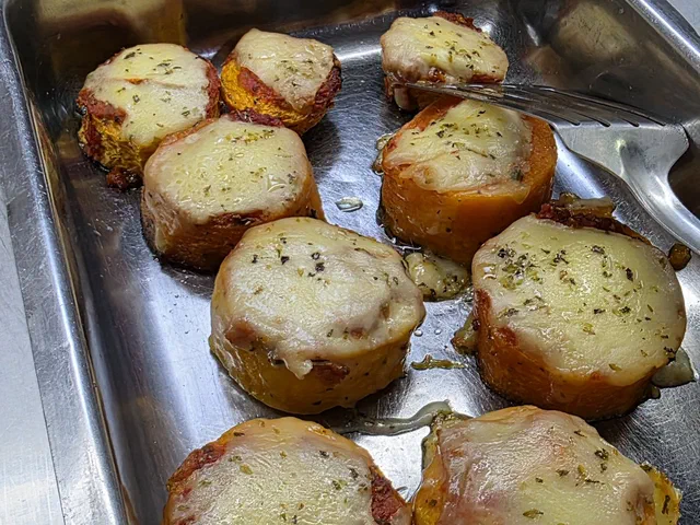 Rondelles épaisses de patate douce cuites au four, couvertes de mozzarella gratinée et d'origan, dans un plat en inox