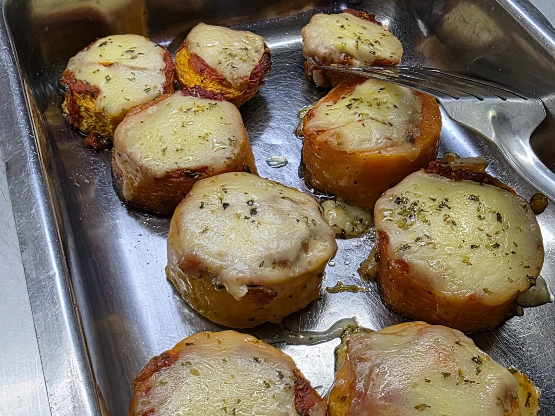 Rondelles épaisses de patate douce cuites au four, couvertes de mozzarella gratinée et d'origan, dans un plat en inox