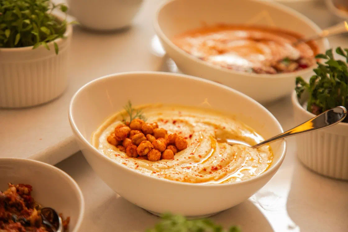 Un bol de houmous lisse garni de pois chiches épicés, d'un filet d'huile et de paprika, entouré d'autres petits bols