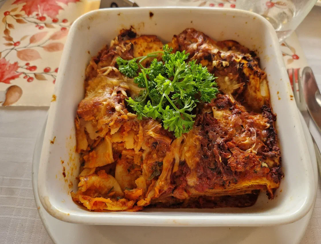Des lasagnes aux légumes gratinées dans un plat carré blanc, décorées d'un bouquet de persil, sur une nappe à motifs d'automne