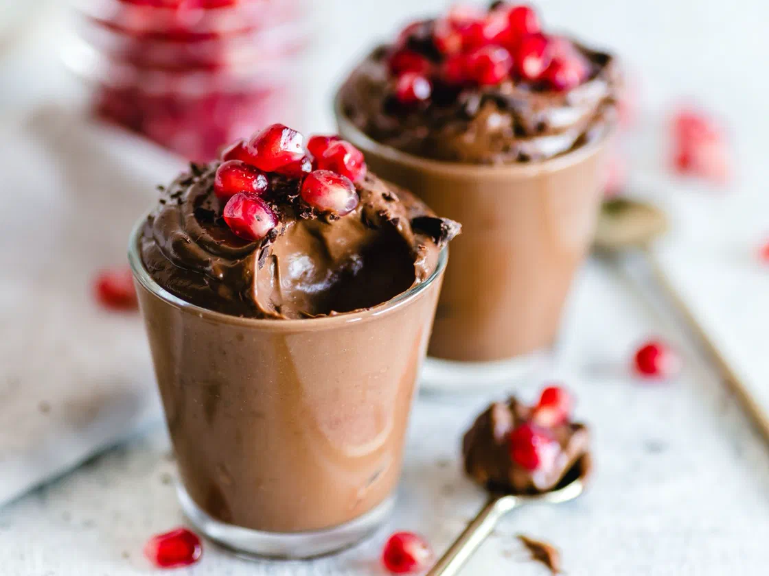 Deux verres de mousse au chocolat garnis de graines de grenade, avec une cuillère de mousse posée à côté