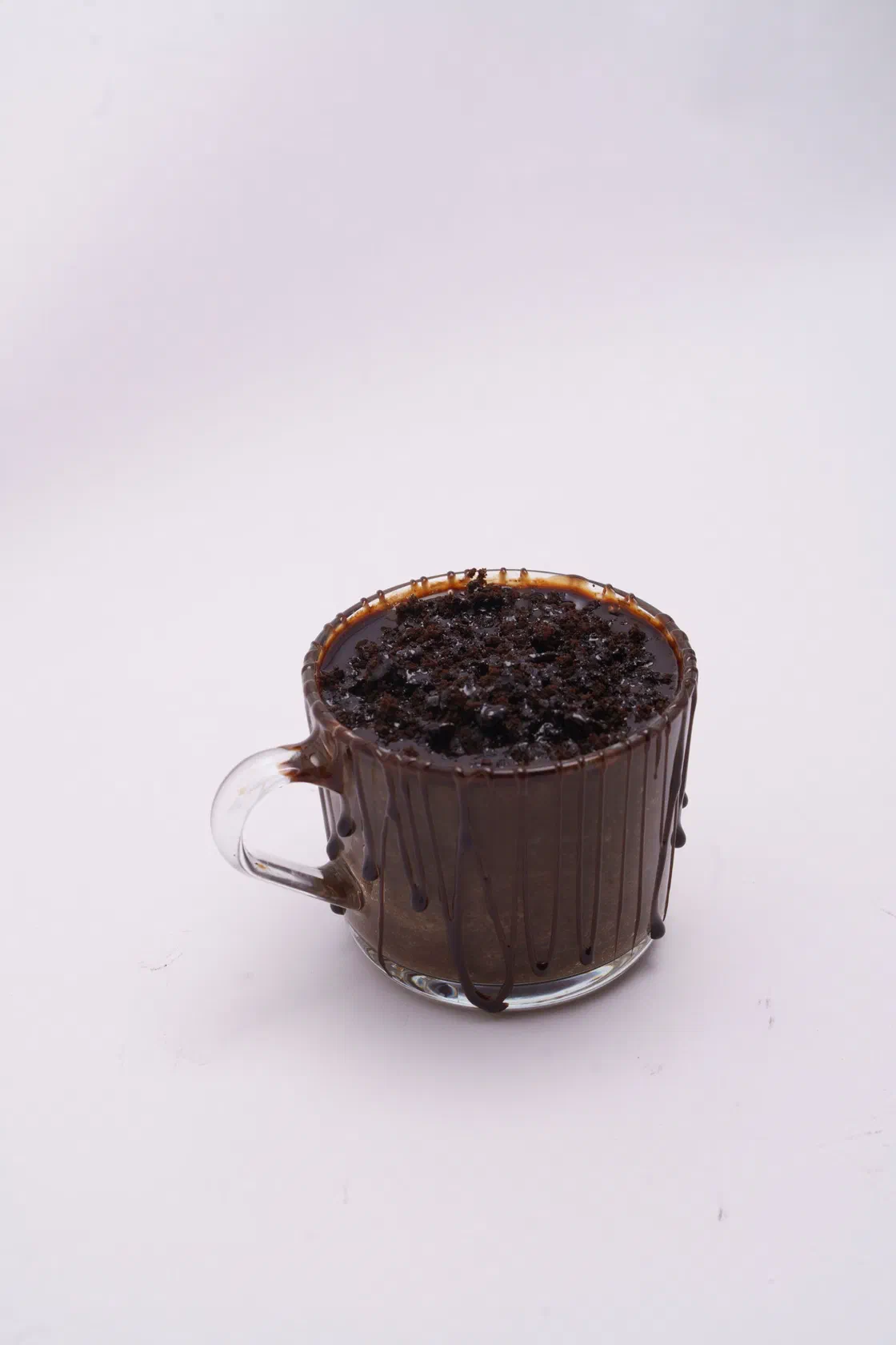 Un mug cake au chocolat dans une tasse en verre, le dessus couvert de copeaux de chocolat, sur fond blanc