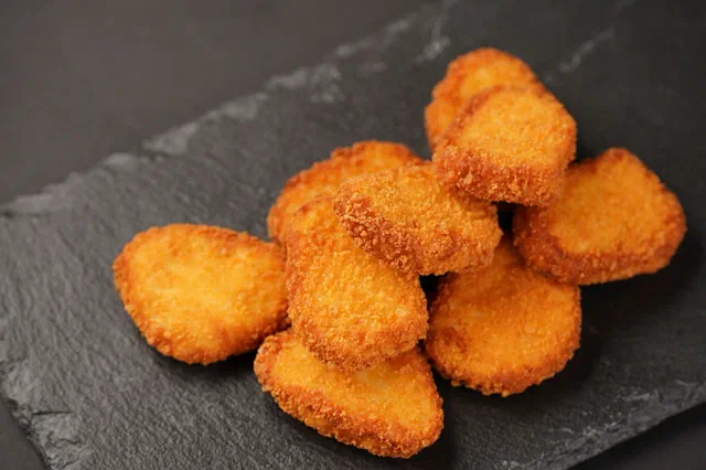 Une dizaine de nuggets de poulet panés et dorés, empilés sur une ardoise noire