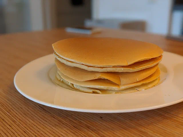 Une pile de pancakes épais et dorés, nature, dans une assiette blanche posée sur une table en bois
