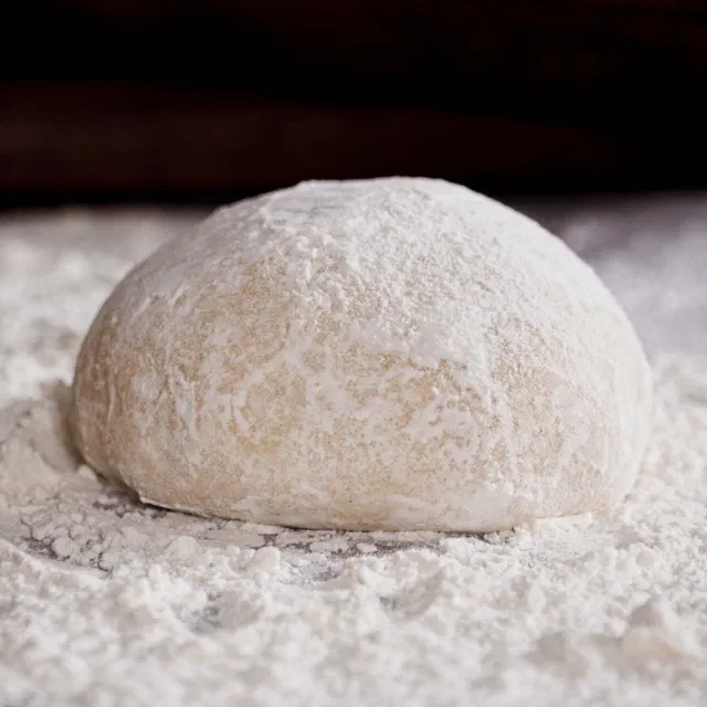Une boule de pâte à pizza levée posée sur un plan de travail fariné