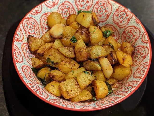 Cubes de pommes de terre rôtis et dorés, parsemés de graines de cumin et de coriandre fraîche, dans un bol à motifs rouges