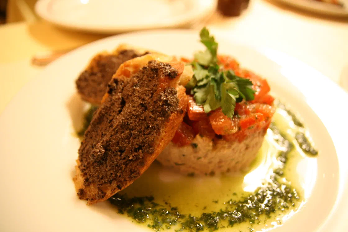 Rillettes de thon moulées en cercle, garnies de tomate en dés et de persil, servies avec des toasts tartinés de tapenade et un filet d'huile au persil