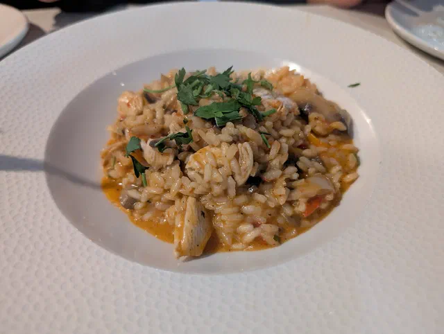 Risotto au poulet et aux champignons dans une assiette creuse blanche, avec du persil plat haché sur le dessus