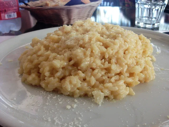 Une assiette blanche de risotto au parmesan, grains crémeux saupoudrés de parmesan râpé