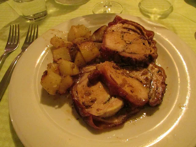 Trois tranches de rôti de porc dans leur jus sur une assiette blanche, avec des dés de pommes de terre rissolées