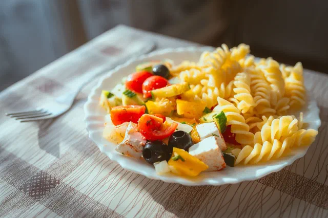 Une assiette de salade de fusilli avec des tomates cerises, des olives noires, des dés de poivron jaune et de fromage blanc