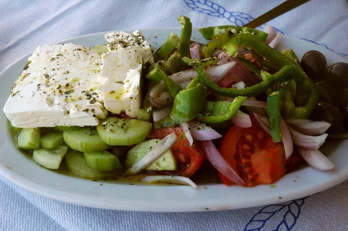 Une salade grecque avec tomates, concombre, poivron vert, oignon et olives, surmontée d'un bloc de feta saupoudré d'origan