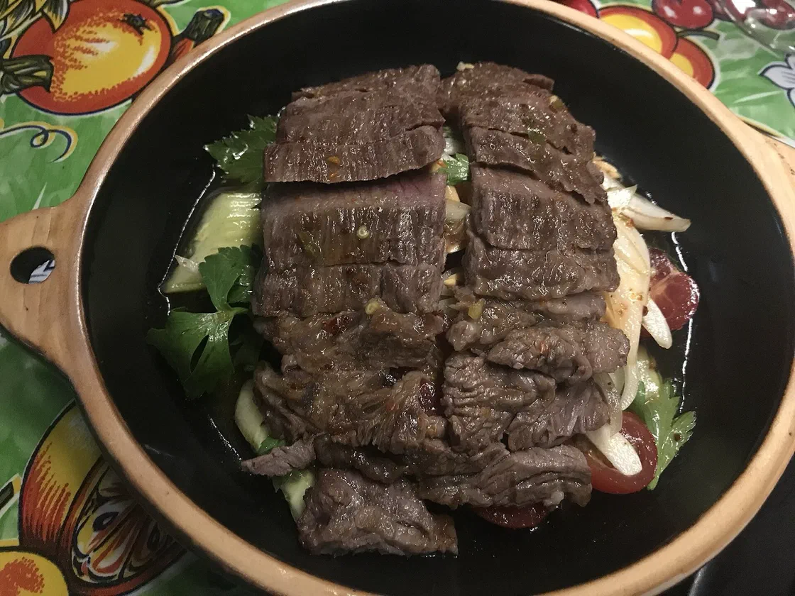 Tranches de bœuf grillé posées sur une salade de concombre, tomates, oignon et coriandre, dans un plat creux en terre cuite