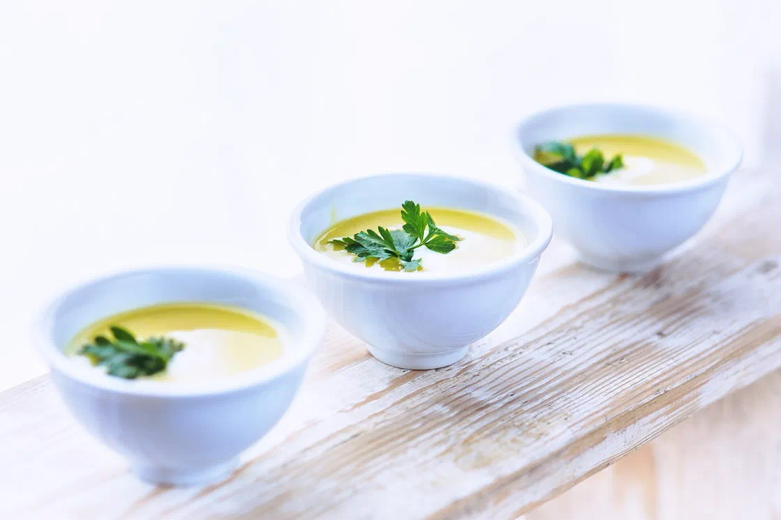 Trois petits bols blancs de soupe poireaux pommes de terre mixée, couleur crème, décorés d'une feuille de persil, sur une planche en bois blanchi