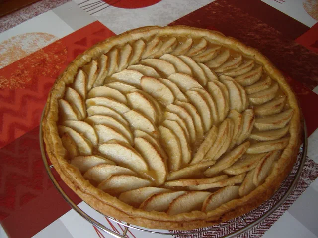 Une tarte aux pommes entière, aux lamelles de pommes dorées disposées en rosace sur une pâte brisée